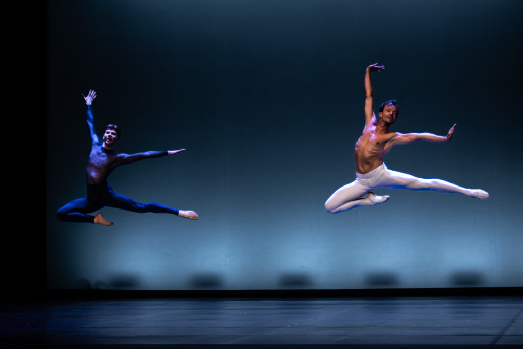 Two dancers leaping simultaneously under the blue light of the Municipal Theatre