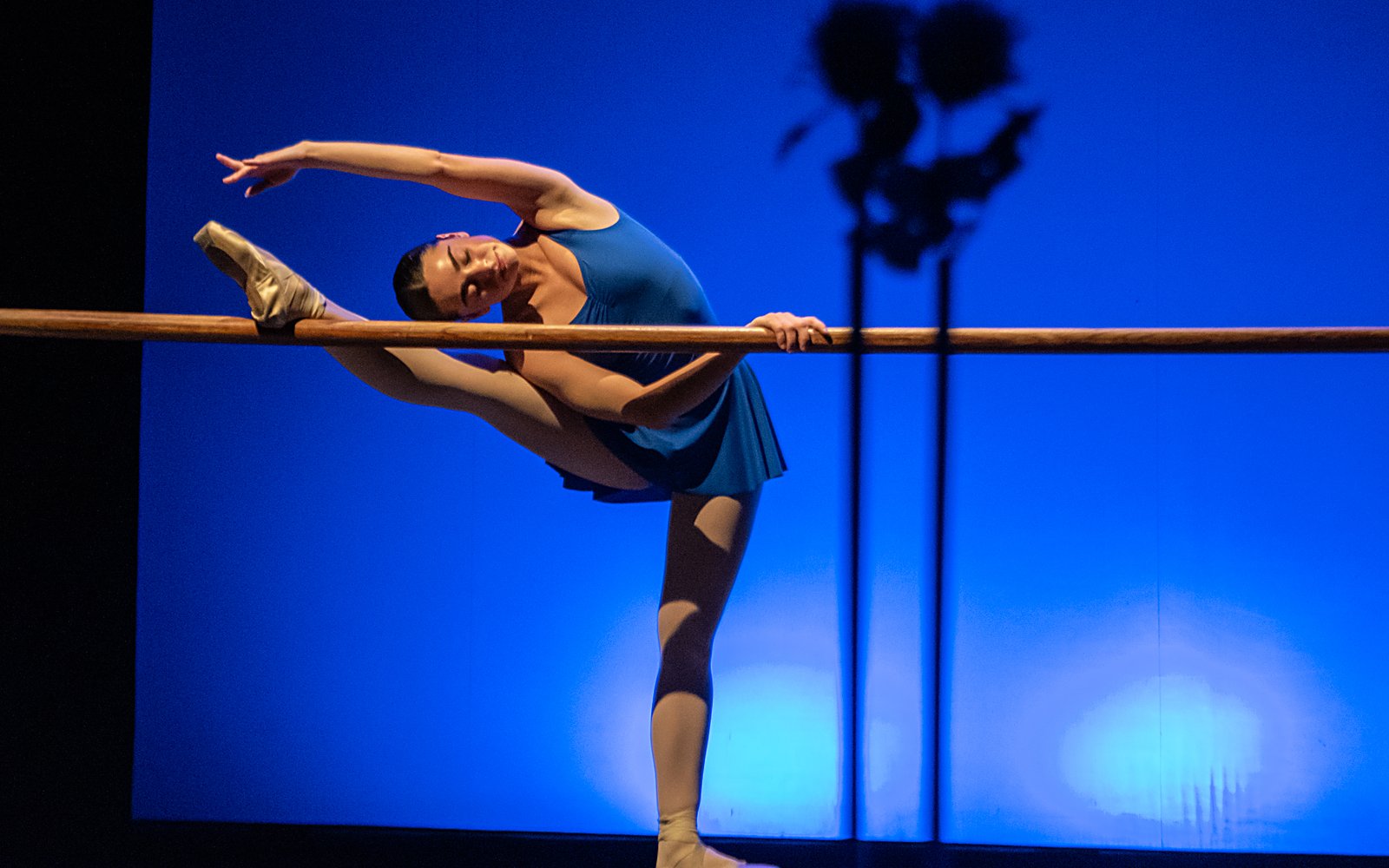 Bailarina de l'escola de dansa de Girona estirant a la barra de ballet, amb llum blava d'escenari