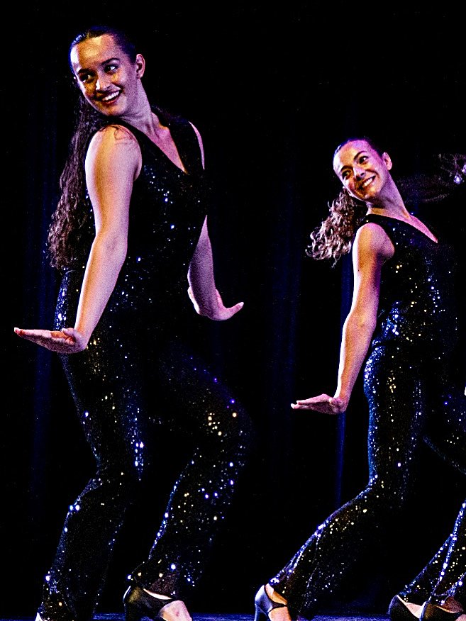 Dues alumnes de jazz ballant amb vestits negres de lluentons al festival de fi de curs