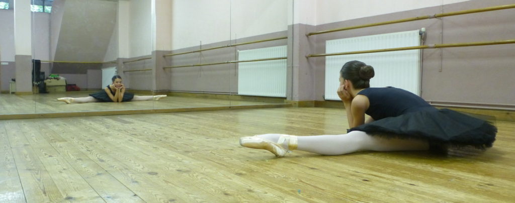 A student stretching in the wood-floored studio, in front of the mirrors